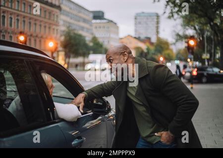 Bald mature man talking to woman sitting in car Stock Photo