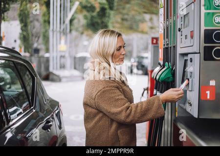 Mature woman doing payment via credit card at fuel station Stock Photo