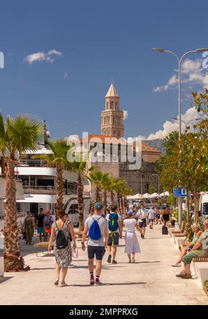 SPLIT, CROATIA, EUROPE - Tourists walk along waterfront. In distance is bell tower of the Cathedral of Saint Domnius. Stock Photo
