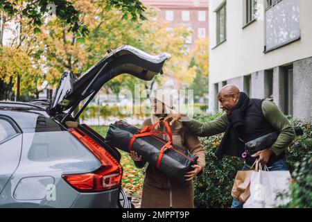 Man assisting woman loading luggage in car trunk while relocating house Stock Photo