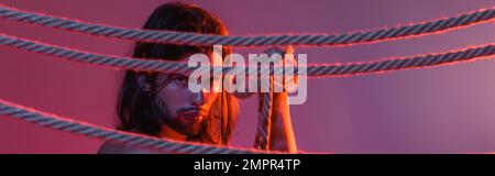 Long haired man holding rope on purple background with light, banner Stock Photo