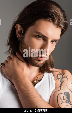 Portrait of long haired tattooed man touching neck isolated on grey Stock Photo