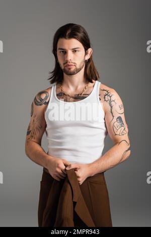 Tattooed long haired man holding jacket standing isolated on grey Stock Photo