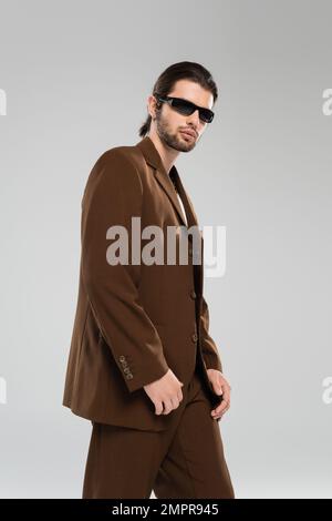 Trendy man in suit and sunglasses standing isolated on grey Stock Photo