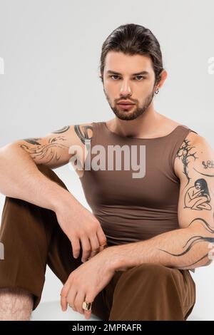 Stylish tattooed man in sleeveless short sitting on grey background Stock Photo
