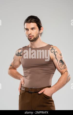 Stylish and tattooed man posing with hand in pocket isolated on grey Stock Photo