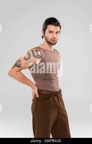 Stylish tattooed man in pants and tank top posing isolated on grey Stock Photo