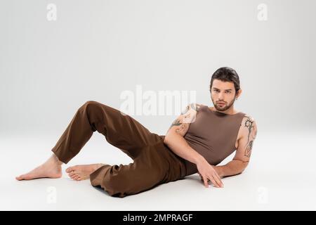 Bearded and tattooed man in sleeveless short posing on grey background Stock Photo