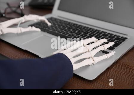 Human skeleton in suit using laptop at table, closeup Stock Photo