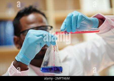Close-up image of scientist pouring red reagent in flask with bue liquid Stock Photo