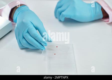 Hands of laboratory worker taking glass plates with drops of bllod Stock Photo