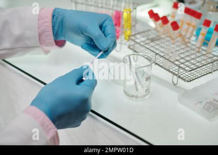 Hands of scientist in gloves using litmus paper when conducting research Stock Photo