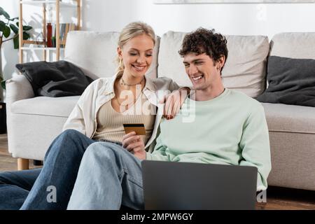 cheerful man holding credit card while using laptop near joyful girlfriend,stock image Stock Photo