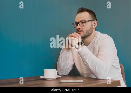 Stylish young brooding fellow businessman from Europe sits back at a table in a cafe. Stock Photo