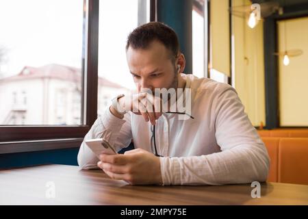 Stylish surprised guy attractive businessman from Europe holds glasses in his hand and looks into his smartphone. Stock Photo