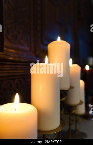 Five large burning white Christmas candles on top of the fire place in front of wooden oak panelling with a lone red candle in the backgroun Stock Photo