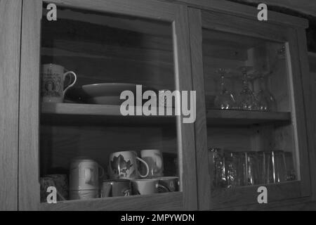 https://l450v.alamy.com/450v/2mpywdn/black-and-white-photo-of-wooden-kitchen-cabinet-with-glass-showing-drinking-glasses-wine-glasses-mugs-cups-and-a-plate-2mpywdn.jpg