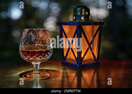 A beautiful cut crystal Brandy Snifter. On a brown marble table in a black background. With a bokeh background. And a lantern light. Stock Photo