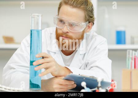 chemist man uses pipette to transfer liquid into bottle glass Stock Photo