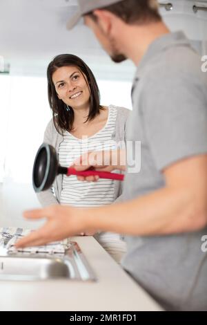 Happy Woman Looking At Male Plumber Using Plunger In The Kitchen Sink,  Stock Photo, Picture And Low Budget Royalty Free Image. Pic. ESY-048550729