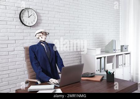 Human skeleton in suit using laptop at table in office Stock Photo
