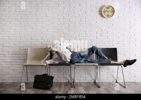Human skeleton in office wear lying on chairs near brick wall indoors Stock Photo
