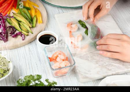 Woman making rice paper roll at white wooden table, closeup Stock Photo