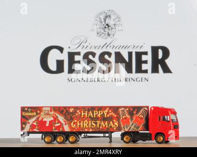 In this photo illustration, a model of a Christmass truck with an Gessener logo  on the background of the company logo on the monitor screen.  The pri Stock Photo