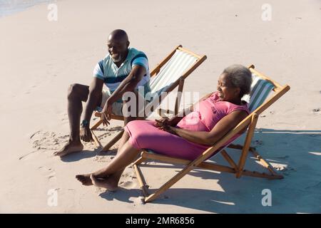 High angle view of happy african american senior couple sitting on deckchairs and talking at beach Stock Photo