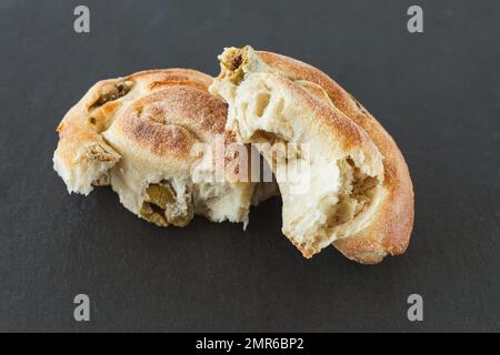 Freshly baked Italian snail bread roll with olives on black background. Broken bread bun, closeup, copy space Stock Photo