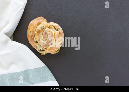 Freshly baked Italian snail bread roll with olives on black background. Bread bun, closeup, copy space Stock Photo