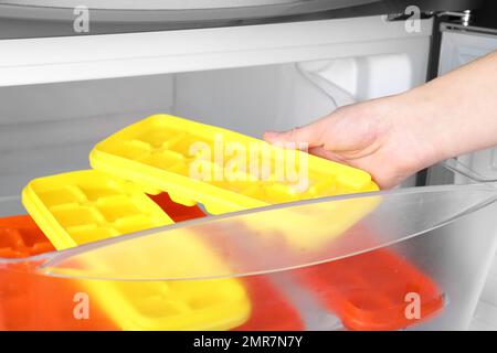 Woman putting tray with citrus fruits frozen in ice cubes into refrigerator  Stock Photo - Alamy