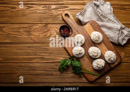 Raw freshly made Khinkali, traditional dish of Georgian Caucasian cuisine, dumplings filled with ground meat on white plate with herbs on wooden rusti Stock Photo