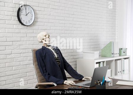 Human skeleton in suit using laptop at table in office Stock Photo
