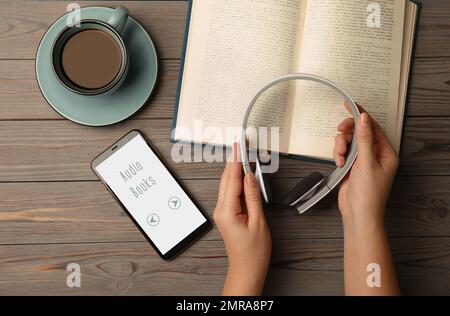 Woman holding headphones over wooden table with book, top view Stock Photo