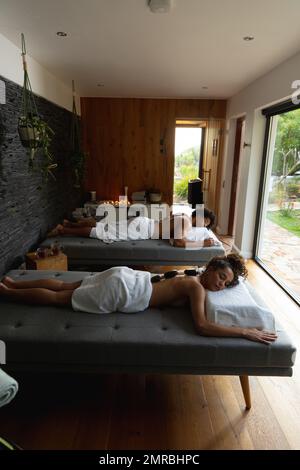 High angle view of biracial young couple with hot stones on backs lying on bed in spa Stock Photo