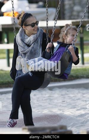 Pregnant Jessica Alba shows off her growing baby bump in a loose fitting grey top as she plays at the park with her daughter Honor Marie, who looked very happy in a trendy denim vest as she held mom's hand to jump down some steps.  Later Alba, who also wore comfy purple sneakers, a swathing grey scarf and held her hair back with a hairband, stayed close by as Honor had a go at the swings. Los Angeles, CA. 03/13/11. Stock Photo