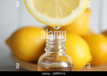 Citrus essential oil dripping from lemon slice into bottle, closeup Stock Photo