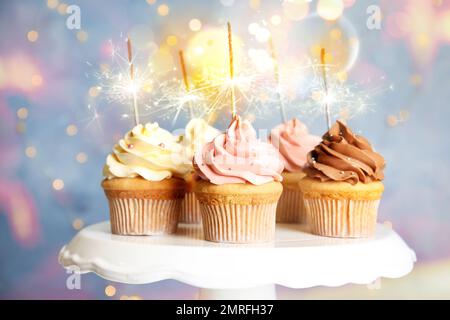 Delicious birthday cupcakes with sparklers on stand against blurred background Stock Photo