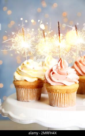 Delicious birthday cupcakes with sparklers on stand against blurred background Stock Photo