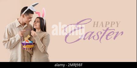 Banner with happy young couple in bunny ears and with Easter eggs in basket on beige background Stock Photo