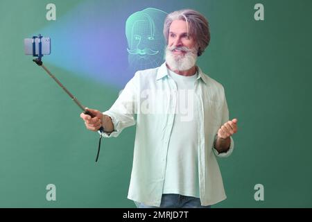 Senior man with mobile phone using facial recognition system on green background Stock Photo