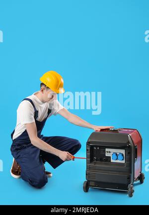 Male worker repairing portable gasoline generator on blue background Stock Photo