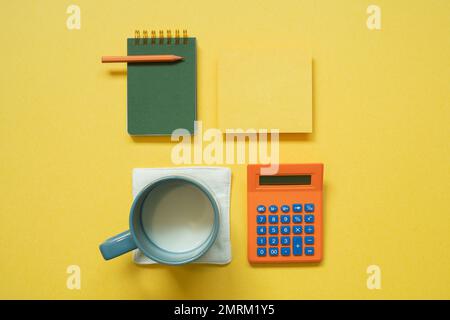 Green notepad, memo paper, color pencil, cup of milk, calculator isolated on yellow background. flat lay, top view, copy space Stock Photo