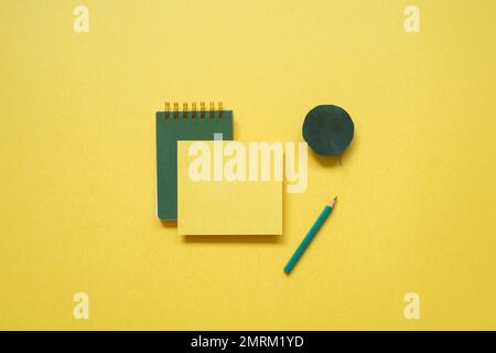 Green notepad, memo paper, color pencil isolated on yellow background. flat lay, top view, copy space Stock Photo