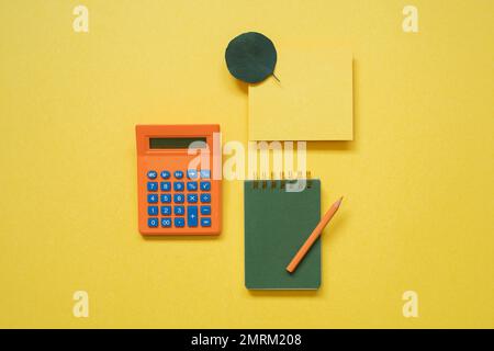 Green notepad, memo paper, color pencil, calculator isolated on yellow background. flat lay, top view, copy space Stock Photo
