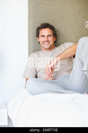Happy man relaxing in bed. Portrait of handsome mature man sitting comfortably on bed. Stock Photo