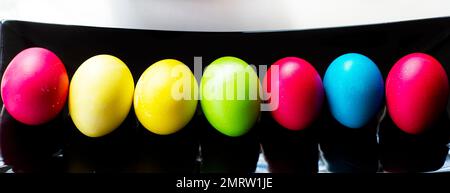 Easter multi-colored eggs in a row on a black rectangular dish. Stock Photo