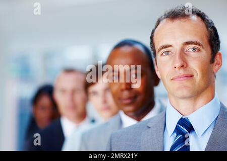Serious team of executives. Focus on executive in foreground with colleagues in distance. Stock Photo