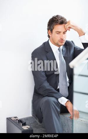 Business man stressed out. Mature business man sitting on the stairs with hand on head. Stock Photo